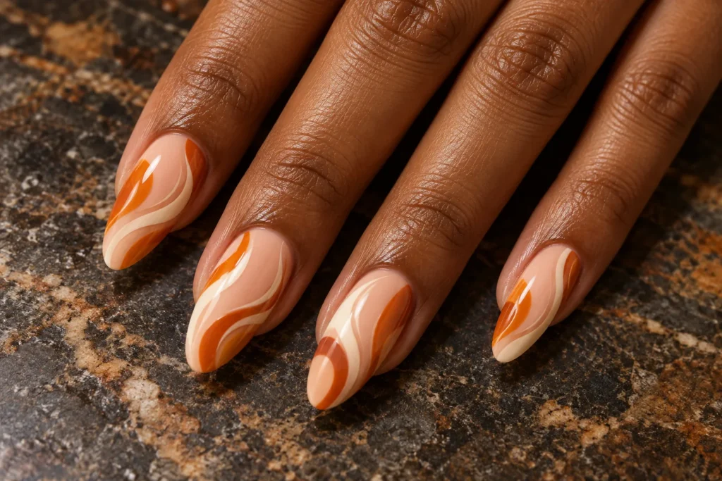 Pumpkin orange and ivory swirls on peach almond nails, close-up against dark stone.