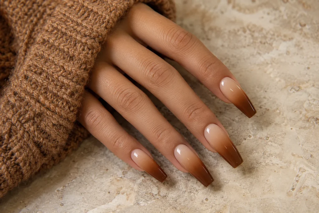 Caramel and nude ombre on long coffin nails, angled view beside a brown knitted sleeve.