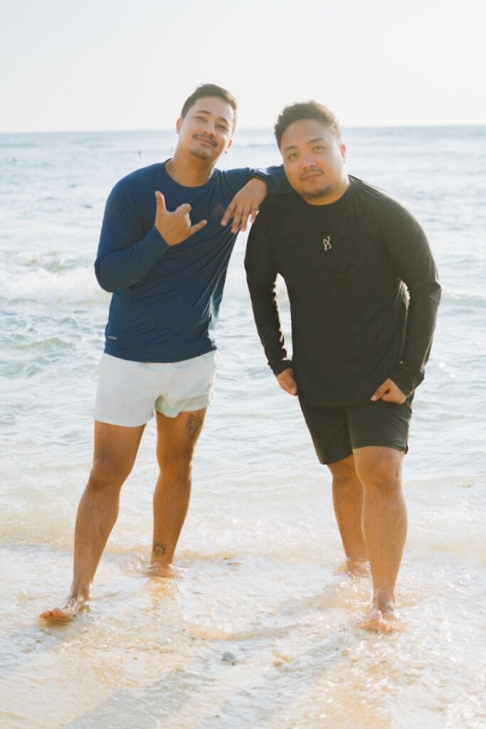 Two men wearing blue and black sweatshirts with shorts at the beach