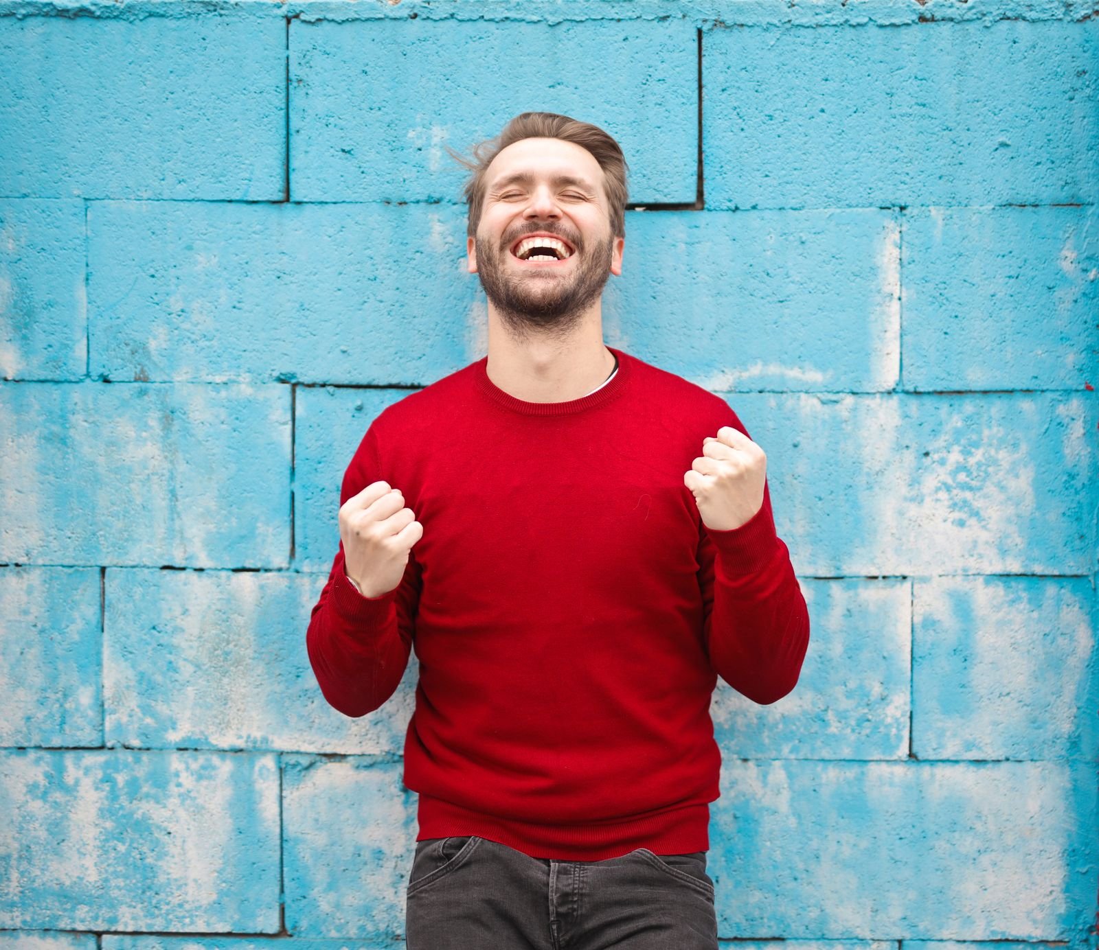Man wearing a red crewneck pullover against a blue wall