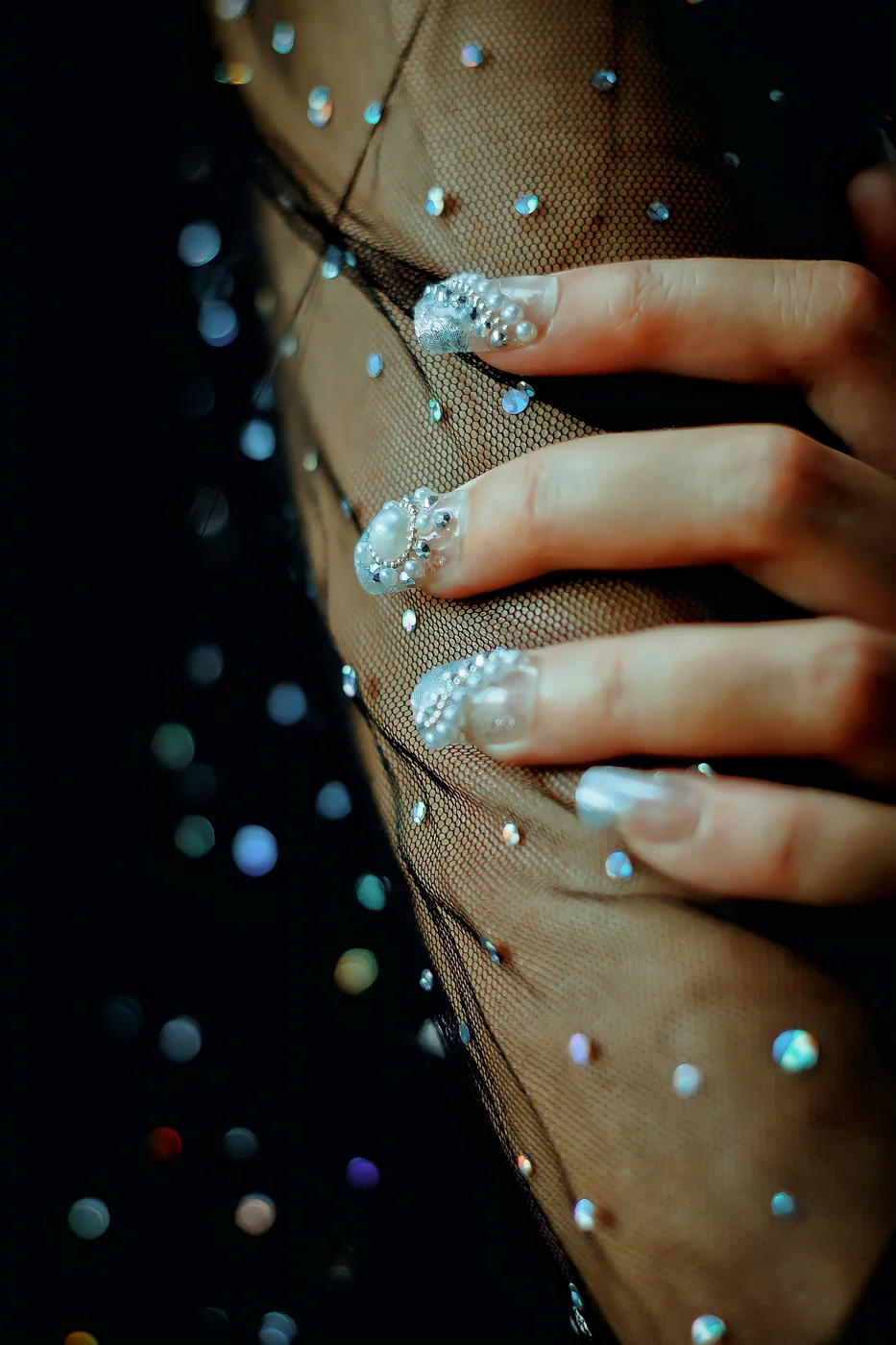 Sparkling embellished nails resting against black mesh fabric