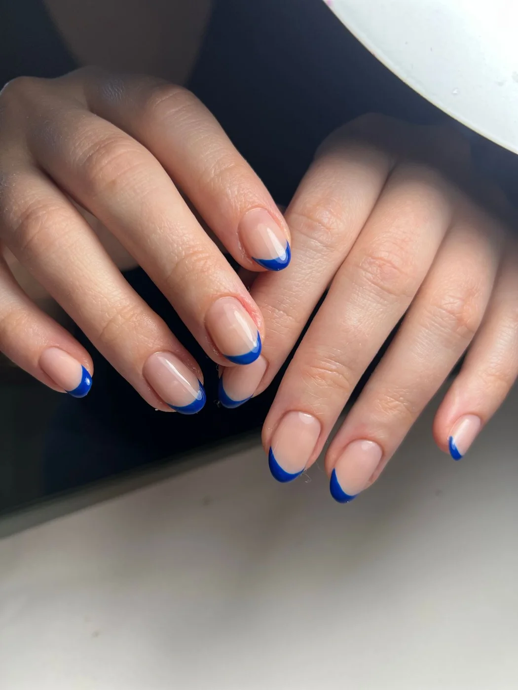 Blue French tips on a sheer pink base viewed across both hands