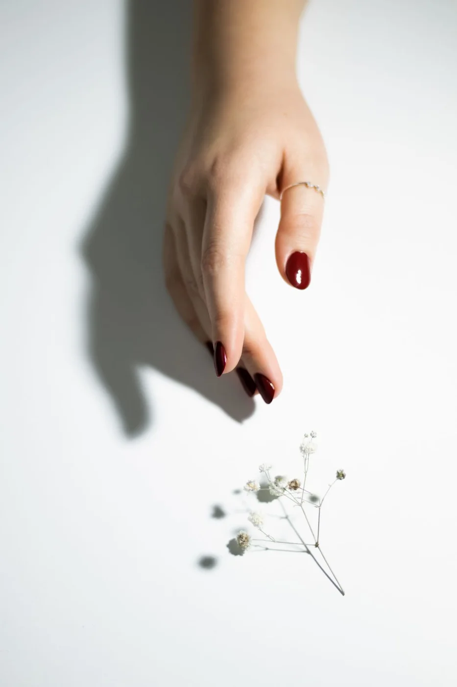 Red polished nails and a ring beside delicate white flowers