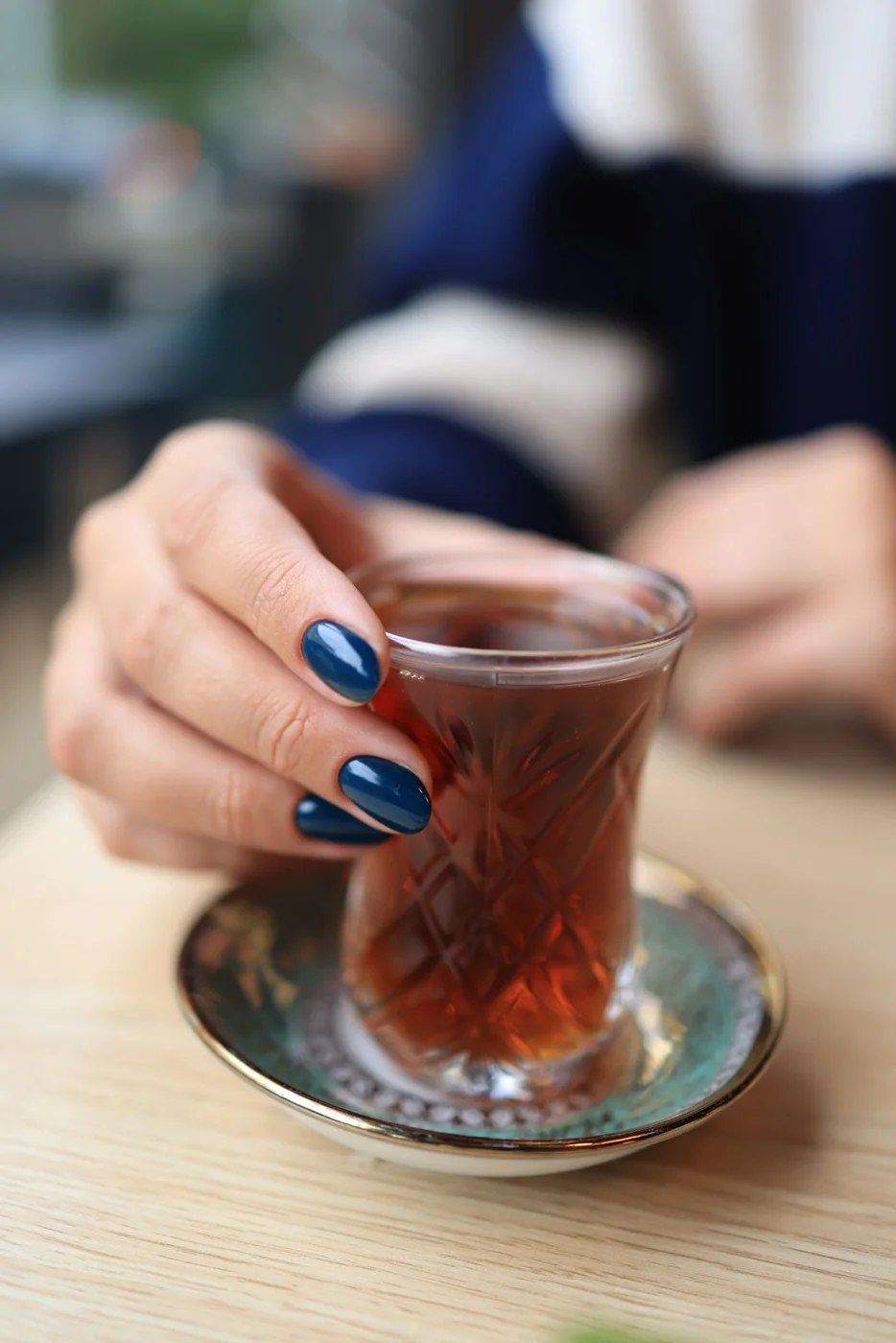 Glossy blue nails holding a glass of tea