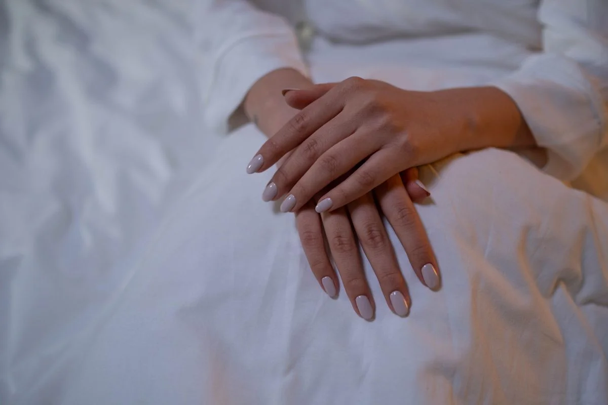 Soft neutral manicure on hands resting over white fabric