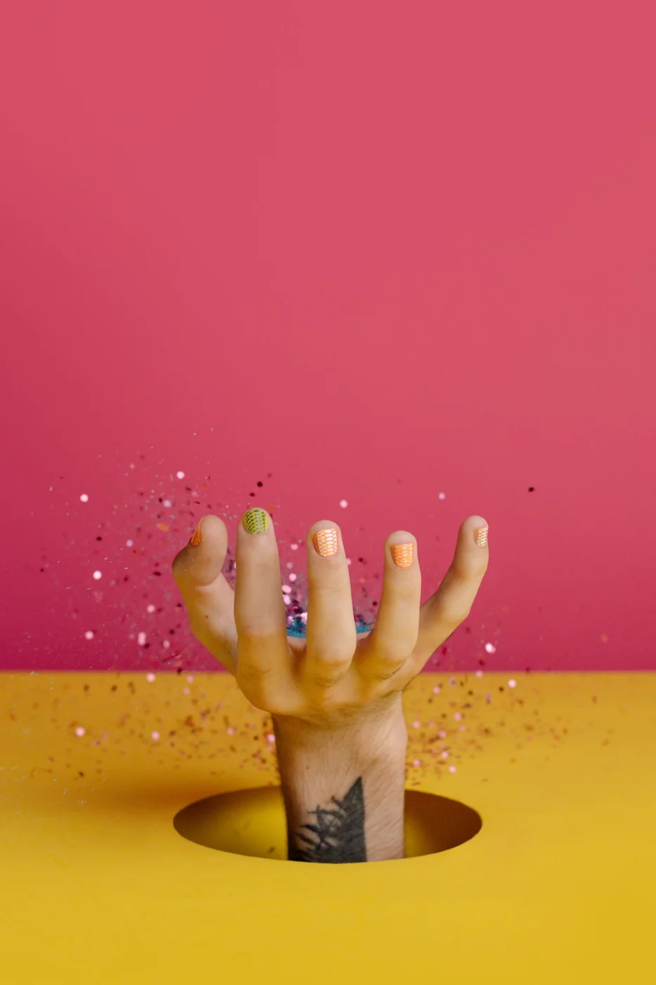 Multicoloured nails reaching through a pink and yellow background