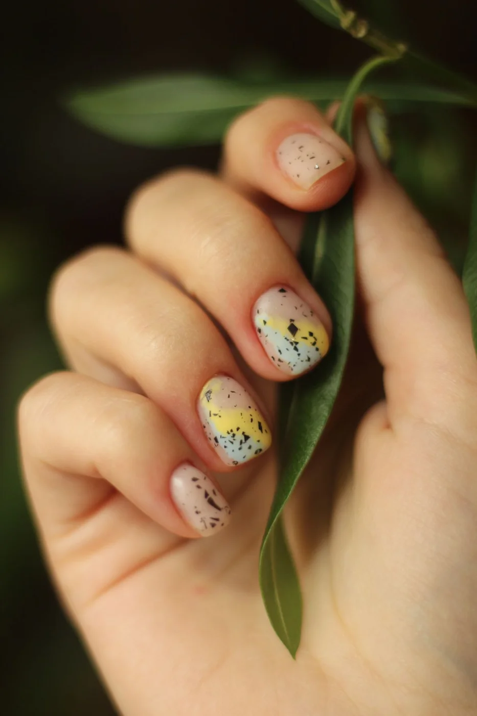 Speckled pastel nail art beside green leaves
