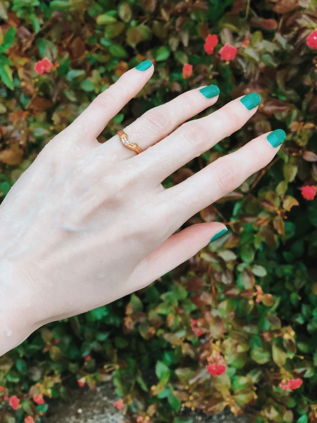 Green manicured nails and a gold ring against green foliage