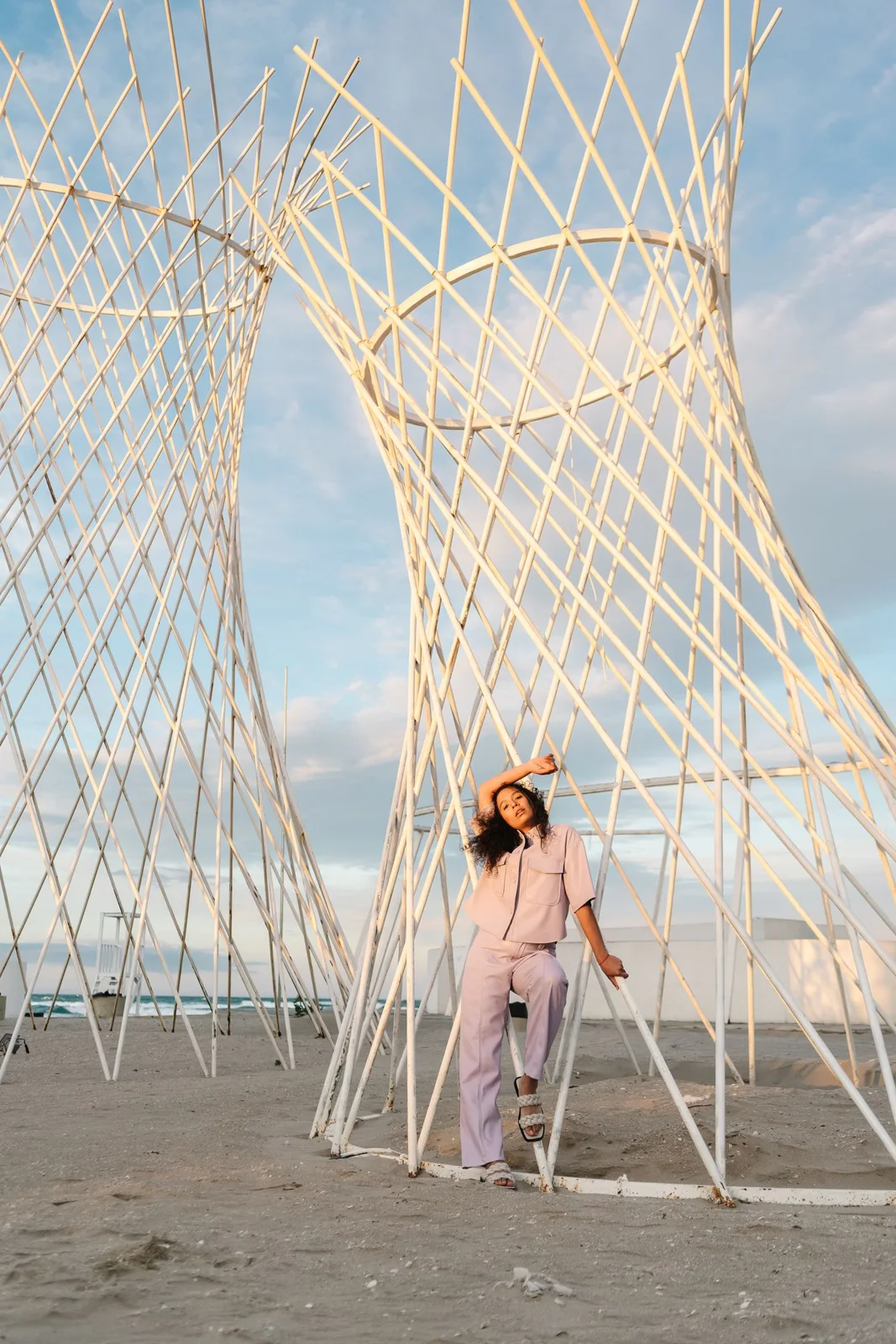 Pastel trouser outfit beside woven sculptures on a beach